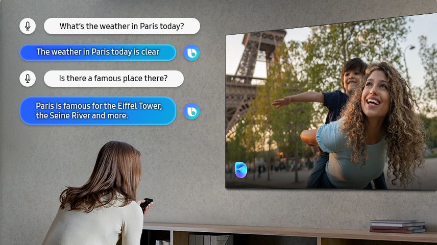Người phụ nữ trong phòng khách nói chuyện với Bixby qua TV. Phụ đề của đoạn hội thoại được hiển thị. Thời tiết ở Paris hôm nay thế nào? Thời tiết ở Paris hôm nay trong xanh. Có địa điểm nổi tiếng nào ở đó không? Paris nổi tiếng với Tháp Eiffel, Sông Seine và nhiều địa điểm khác.