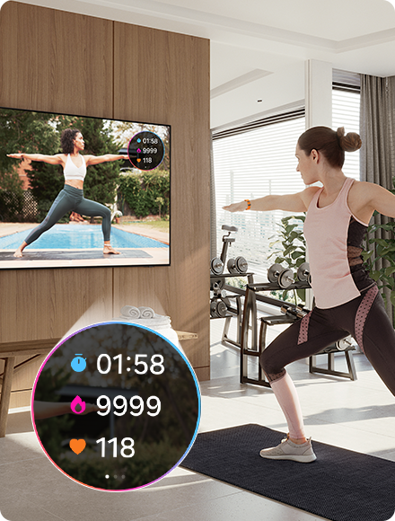 Una mujer hace yoga mientras mira a un entrenador en la TV. La TV también muestra estadísticas de ejercicio 01:58, 9999, 118 desde el Galaxy Watch conectado.