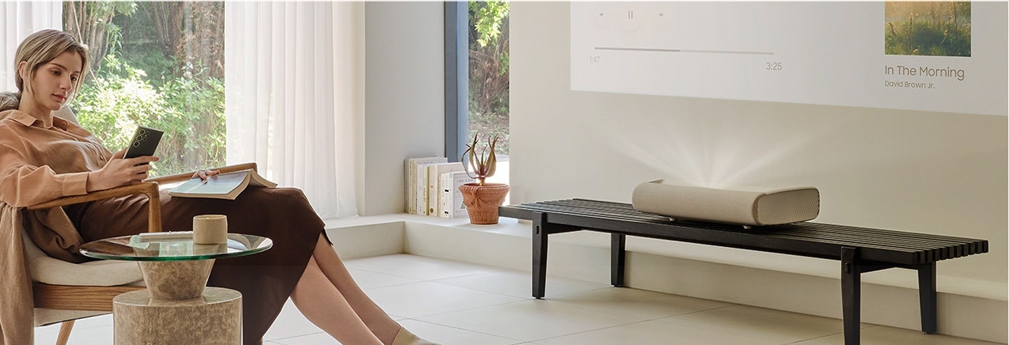 A woman relaxing in her living room casts music from her mobile device to the Premiere. The music is displayed on the wall.